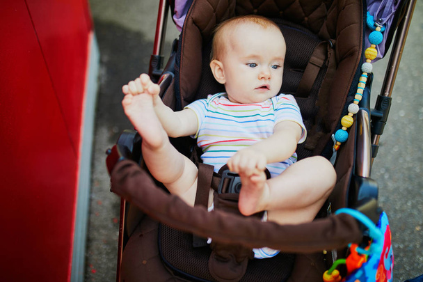 Baby girl with colorful toys in stroller. Little child in pram. Infant kid outdoors in pushchair - Foto, afbeelding