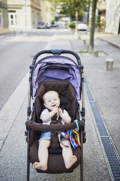 Baby girl with colorful toys in stroller. Little child in pram. Infant kid outdoors in pushchair - Fotoğraf, Görsel