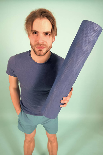 Man hold yoga mat. Fashion athlete in blue tshirt and shorts. Sportsman with stylish bristle and hair. Gym equipment for training and workout. Yoga or pilates and sport activity - Φωτογραφία, εικόνα