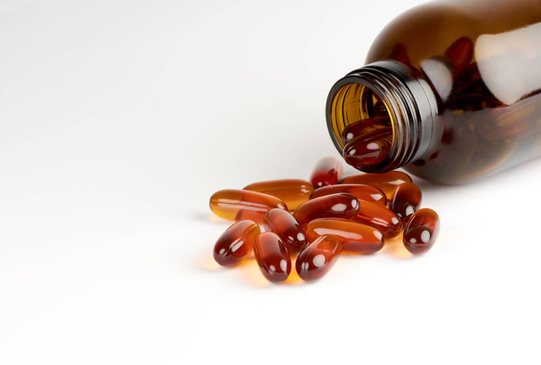 Close-up view of orange pills or lecithin capsules in a brown glass bottle on a white background with space for text - Photo, Image