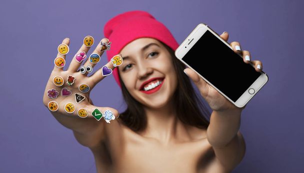 Mulher com emoji móvel social popular sorri adesivos para celular em suas mãos feliz sorrindo rindo mostrando tela de exibição em branco
 - Foto, Imagem