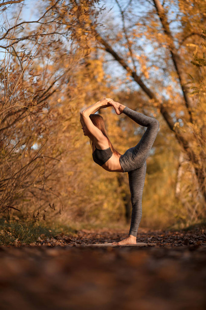Young woman practicing yoga exercise in autumn park with yellow leaves. Sports and recreation lifestyle. - Foto, Imagem