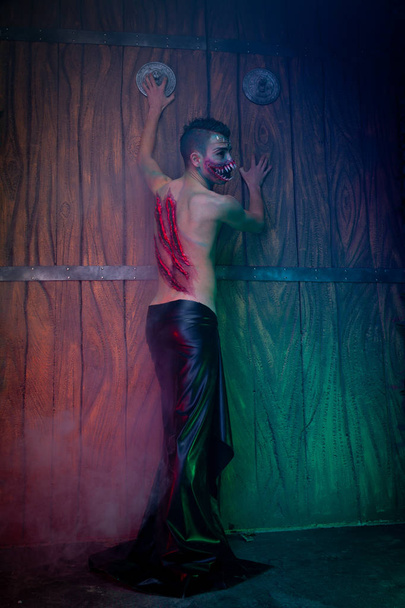 scary vampire male with huge teeth and bloody body as halloween body art standing in the night smoke alone - Fotografie, Obrázek