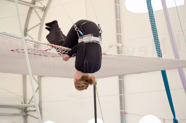 Dospělá samice přistane na netu, příprava k odpojení na na létající hrazdě školu v kryté tělocvičně. Žena je amatérský umělec trapeze. - Fotografie, Obrázek