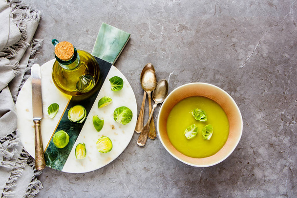 Seasonal Brussels sprouts vegetable cream soup with spices in bowl and Raw Brussel sprouts over grey concrete table background flat lay. Vegan, vegetarian, healthy, dieting food concept - Image - Foto, Imagen