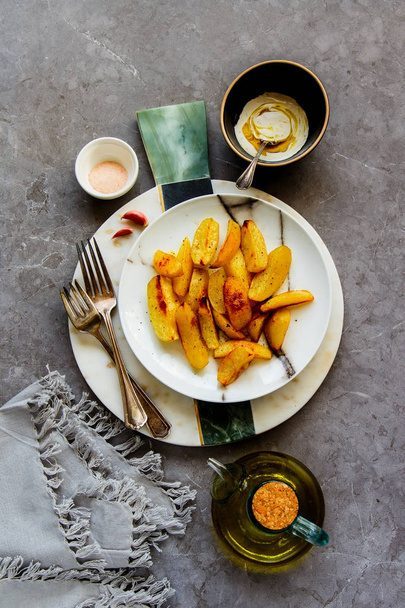 Delicious Fried potato wedges in plate with salt, garlic and white sauce over grey concrete table background. Flat lay, top view - Image - Foto, Imagen