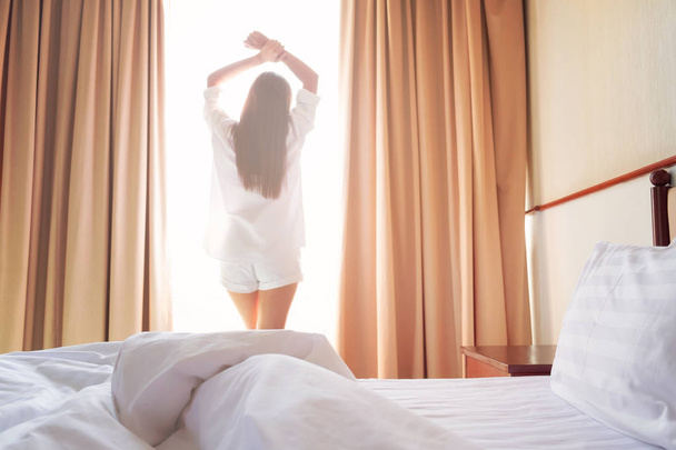 Жінка розтягується в ліжку після пробудження. М'яке світло і м'який фокус, щоб відчувати себе розслабленим і комфортним
.  - Фото, зображення