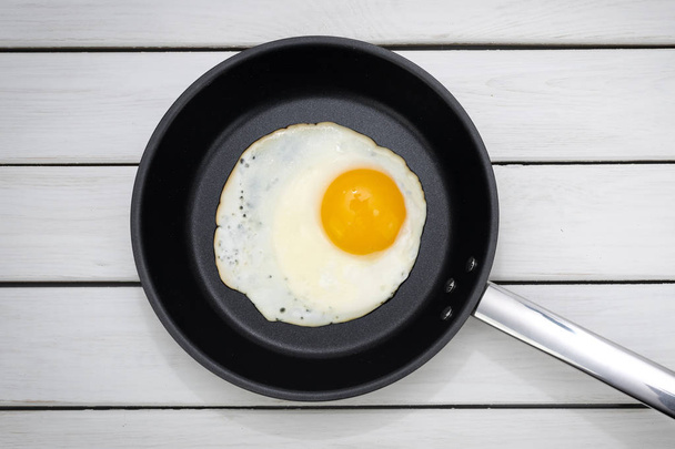 Top view of a sunny side up fried egg in a black pan on wooden white table.  - Fotó, kép