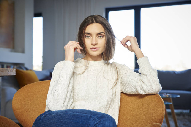 Portrait of young woman with beautiful smiling wearing casual clothes while relaxing in armchair at home.  - Foto, Bild