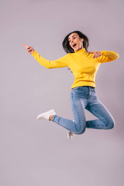 Beautiful excited happy young brunette woman in yellow is jumping isolated on grey background - Fotoğraf, Görsel
