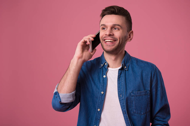 Handsome modern casual man is talking on smart phone isolated on pink background - Foto, afbeelding
