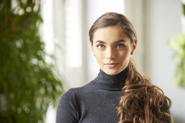 Close-up portrait of beautiful young woman wearing roll neck sweater while  smiling indoor. - Fotoğraf, Görsel