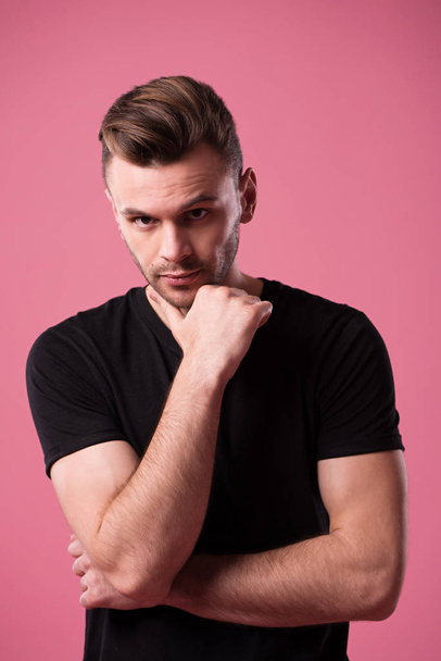 Beautiful stylish confident and serious man in black t-shirt is posing on pink background - Foto, Imagem