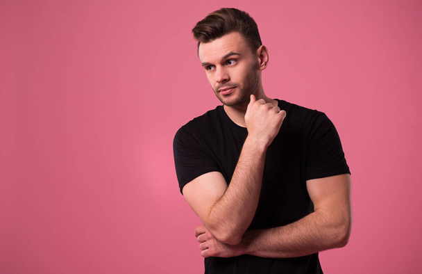 Beautiful stylish confident and serious man in black t-shirt is posing on pink background - Foto, immagini