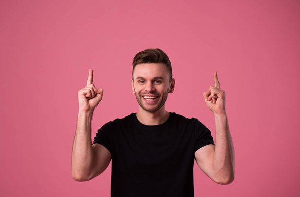 Happy handsome young man portrait in black t-shirt isolated on pink wall - Foto, afbeelding