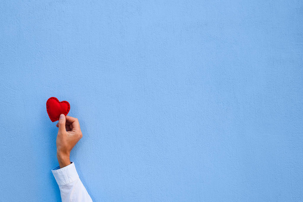 Coração de Valentim vermelho na mão de um homem no fundo da parede azul. Cartão de saudação com espaço de cópia para texto
 - Foto, Imagem