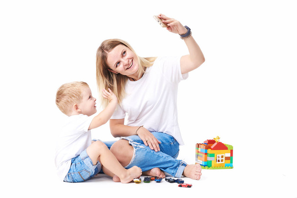 Happy mother laughing taking selfie with little son on smartphone, smiling single mom and cute adopted boy playing making photo posing for self portrait, mommy and kid watching video on cell  - Foto, Imagen