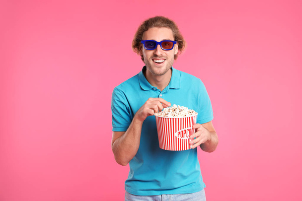 Man with 3D glasses and popcorn during cinema show on color background - Foto, Bild