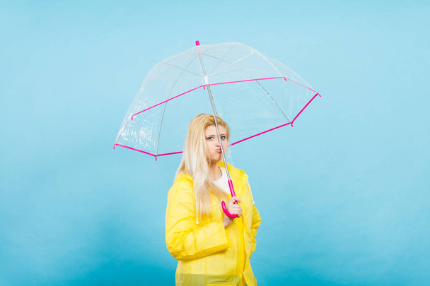 Sad bored blonde woman wearing yellow raincoat holding transparent umbrella waiting for rain. - Fotó, kép
