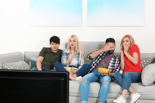 Young people with snacks watching TV on sofa at home - Foto, Bild
