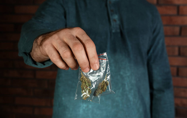 Male dealer holding hemp in plastic bag near brick wall, closeup - Foto, immagini