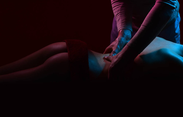 Close-up masseur hands doing back massage in spa center. Female patient is receiving treatment by professional therapis. Sexy ass, couple at home. - Φωτογραφία, εικόνα