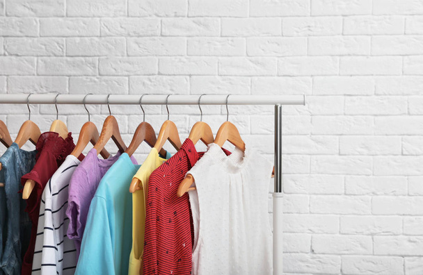 Wardrobe rack with stylish clothes near brick wall indoors. Space for text - Foto, Imagen