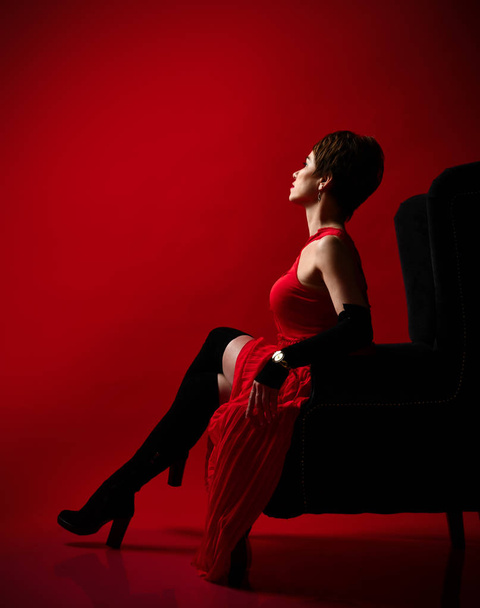 Portrait of a professional short hair business woman in red dress and long boots on red  - Fotó, kép