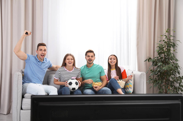 Group of people with snacks and ball watching soccer match on TV at home - Фото, изображение