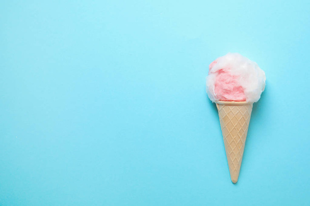 Ice cream cone with fluffy cotton candy and space for text on color background, top view - Foto, imagen