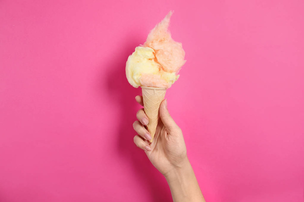 Woman holding ice cream cone with fluffy cotton candy on color background, closeup - Foto, Bild
