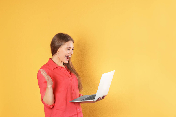 Emotional young woman with laptop celebrating victory on color background. Space for text - Foto, Bild