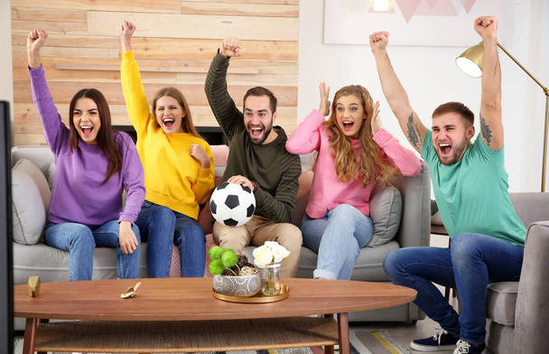 Group of friends celebrating victory of favorite soccer team in living room - Фото, изображение