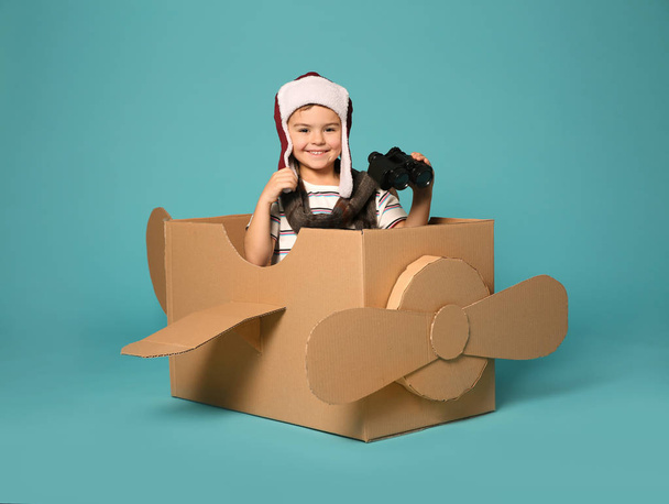 Cute little boy playing with binoculars and cardboard airplane on color background - Foto, afbeelding