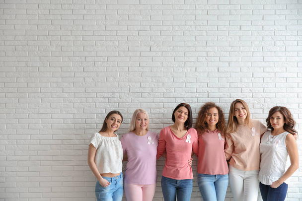 Group of women with silk ribbons near brick wall, space for text. Breast cancer awareness concept - Фото, изображение