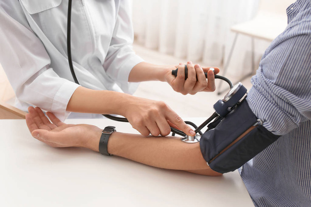 Doctor checking patient's blood pressure in hospital, closeup. Cardiology concept - Photo, image