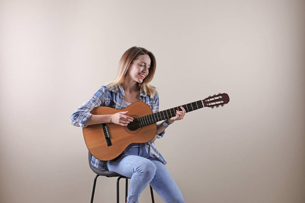 Young woman playing acoustic guitar on grey background - Valokuva, kuva
