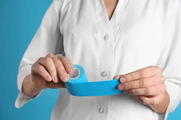 Female doctor holding elastic therapeutic tape on color background, closeup. Medical object - Foto, imagen
