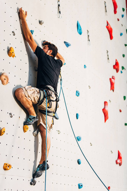 Άντρας που φοράει σχοινί, σκαρφαλώνει σε έναν πολύ ψηλό τοίχο αναρρίχησης. - Φωτογραφία, εικόνα