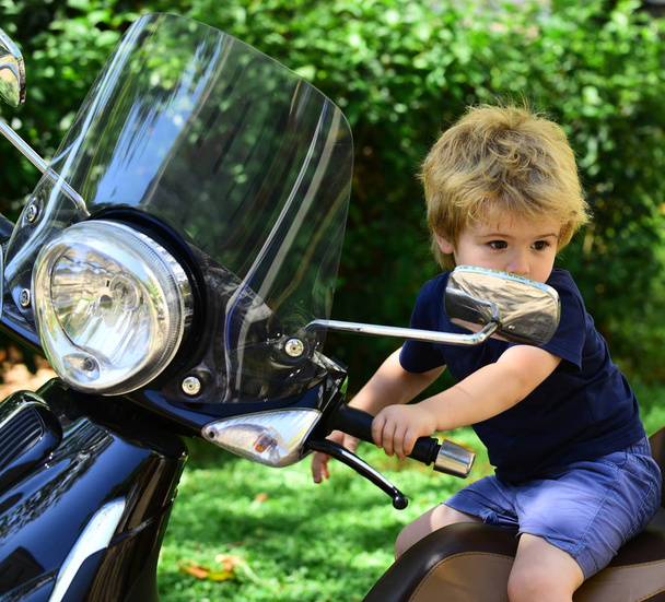 Journey. Sad blond boy on motorbike. Little boy on street. Black motorbike on natural background. Daily walk with child. Traveling with children. Transport and driving - Photo, Image