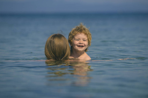 Felices vacaciones juntos. Actividades familiares. Sonriente niño lindo mira a la cámara desde el mar. Emociones alegres del niño con su madre. Día soleado para nadar en el mar
 - Foto, Imagen