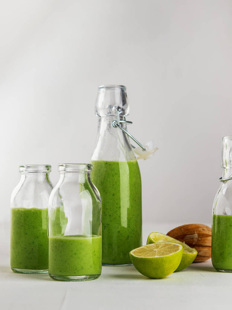 Fresh made healthy green smoothie served in bottles on white background. Fruits and vegetables and seeds ingredients around. Close with copy space. Lifestyle. Vertical. - Foto, immagini