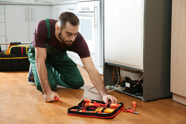Male technician in uniform repairing refrigerator indoors - 写真・画像