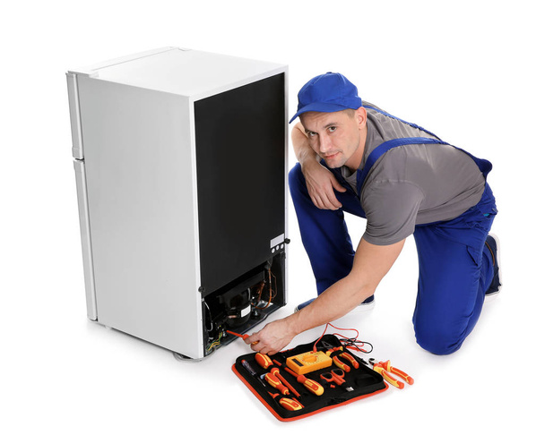 Male technician in uniform repairing refrigerator on white background - Photo, image