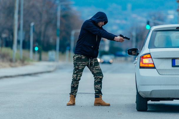 El ladrón de coches está sacando al dueño del coche de su coche y tratando de conseguir el coche mientras apunta con un arma cargada a la cabeza de los conductores
. - Foto, Imagen