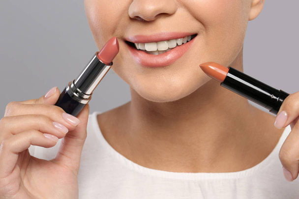 Young woman with lipsticks on gray background, closeup - Photo, image