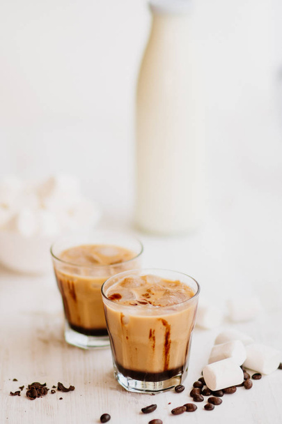 Marshmelow and coffee beans on the table. Concept of a cooling drink. Summer drink. Cold coffee with milk and chocolate. Vertical shot. Light background. Iced coffee. - Фото, изображение