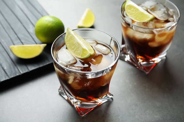 Glasses of cocktail with cola, ice and cut lime on grey background - Foto, Imagem