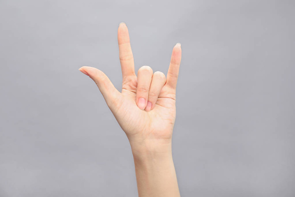 Γυναίκα που δείχνει χέρι σύμβολο σε γκρι φόντο, κινηματογράφηση σε πρώτο πλάνο. Γλώσσα του σώματος - Φωτογραφία, εικόνα