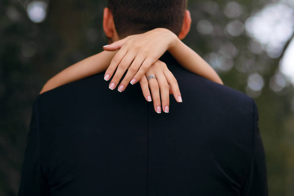 the girl embraces the neck of the groom, the beautiful bride walks in the park with the groom, on her finger ring. - Foto, imagen